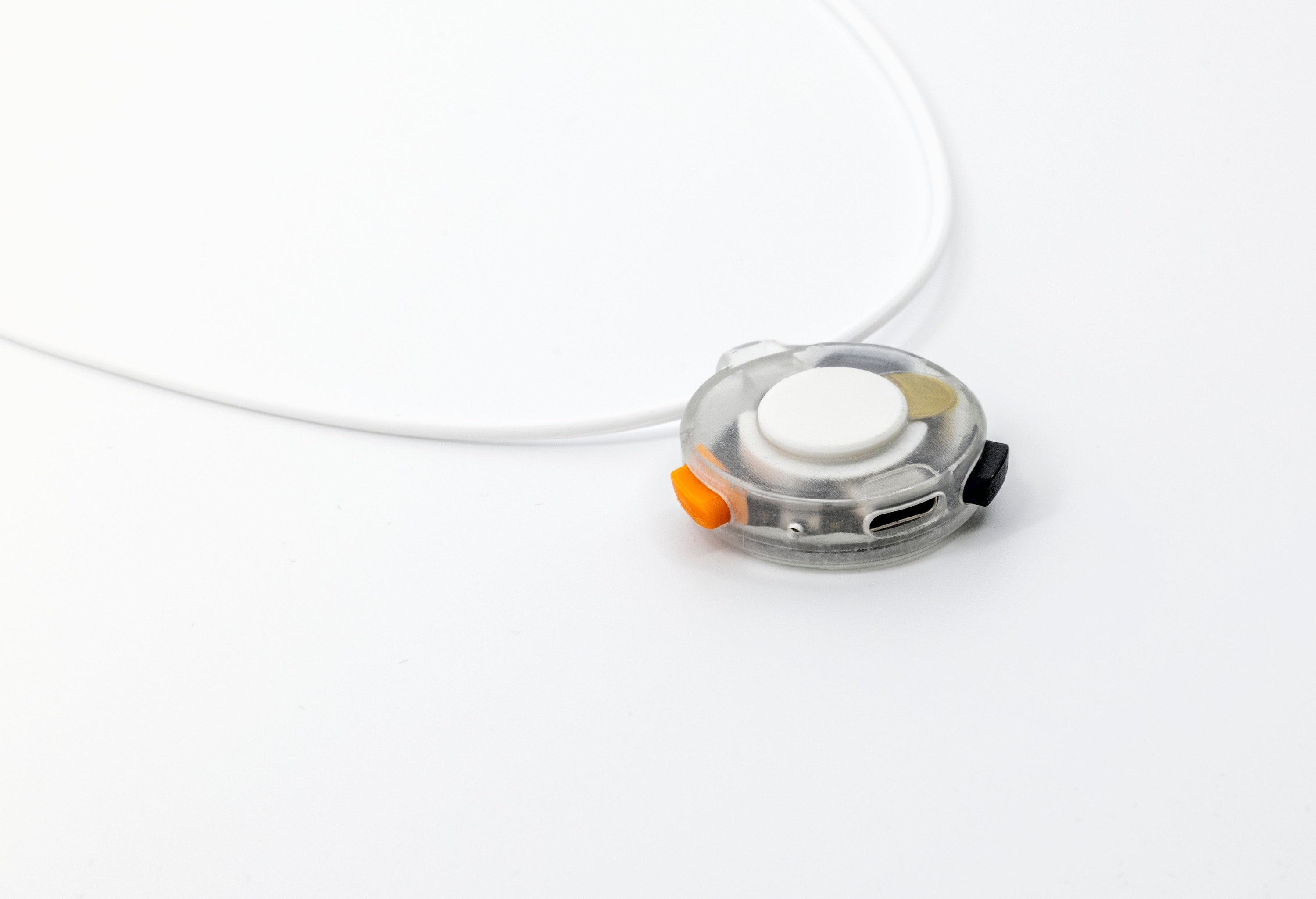 Close-up of VOX on its cord: the capture button on top, the orange and dark side controls, the skin-contact microphone, and the USB-C charging port along the edge.